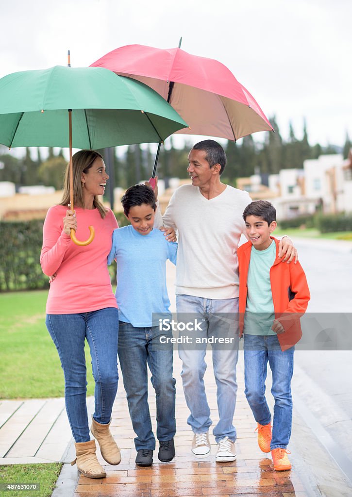 Family walking under the rain holding umbrellas Happy family walking outdoors under the rain holding umbrellas Family Stock Photo