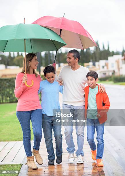 Family Walking Under The Rain Holding Umbrellas Stock Photo - Download Image Now - Family, Rain, Umbrella