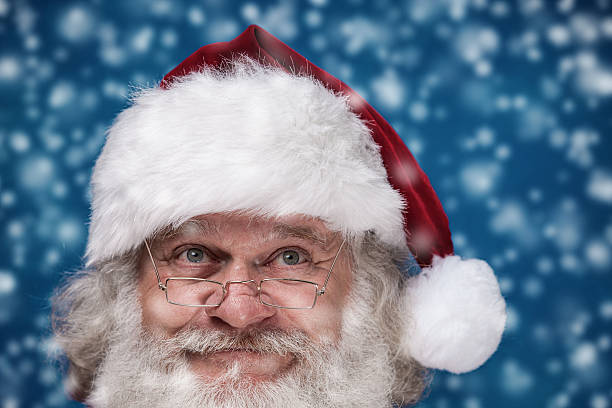 Closeup of the face of authentic Santa Claus with a real beard, looking up at the falling snow with a thoughtful little smile.