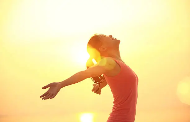 Photo of cheering woman open arms under  sunrise on beach