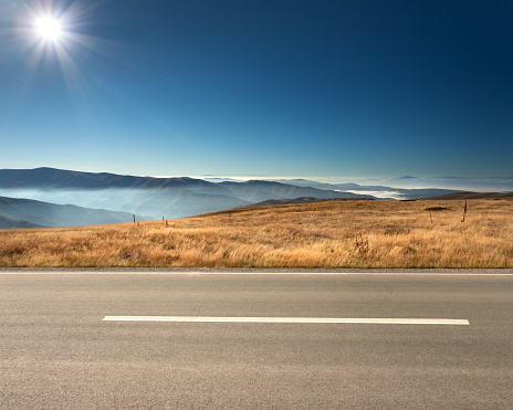 Side view of empty asphalt road and cloudy mountains in background at idyllic sunny day.
