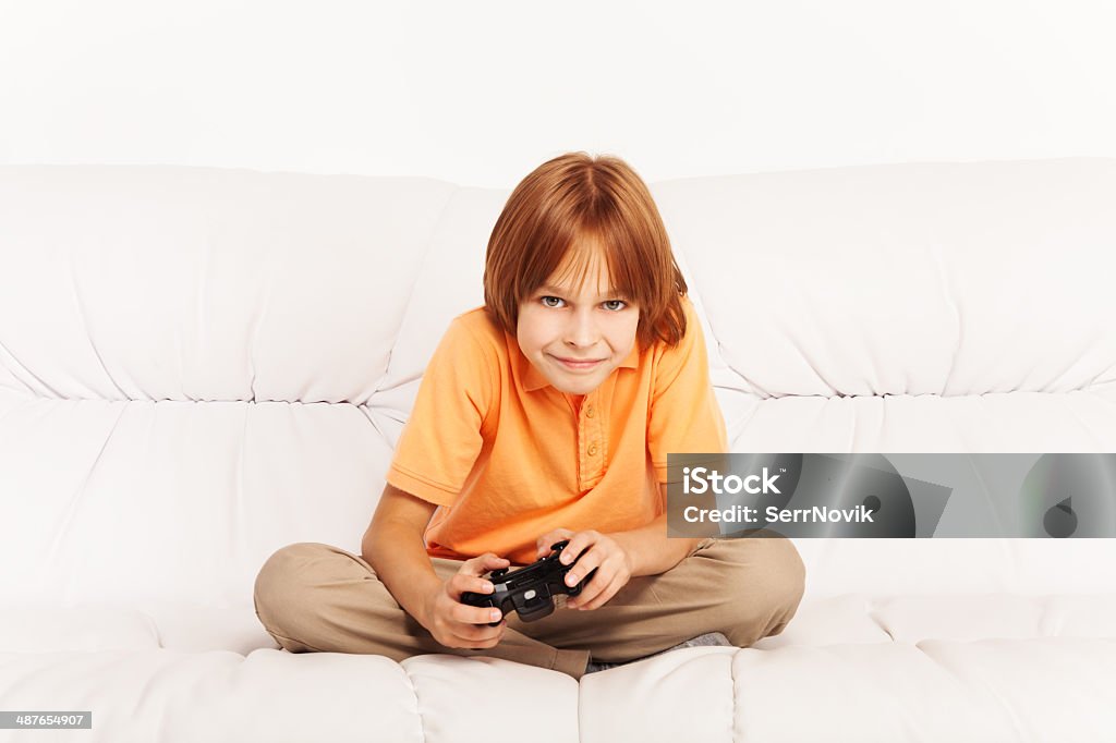 Boy playing video game Happy Caucasian boy playing video games holding game controller sitting on the coach in living room Child Stock Photo