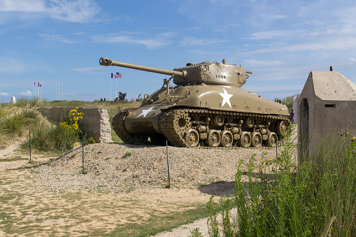 Sainte-Marie-du-Mont, France - july 28 2014. M4 Sherman tank breaching the atlantikwall in Sainte-Marie-du-Mont, france. Unidentified people in the background looking at a monument.