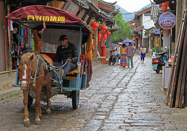 man is driving horse-drawn vehicle  in Lijiang, China Lijiang, China - June 11, 2015: man is driving horse-drawn vehicle  in Lijiang, China blind arcade stock pictures, royalty-free photos & images