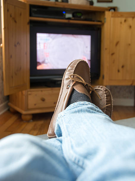 istock Man's feet with slippers with television in the background 487673108