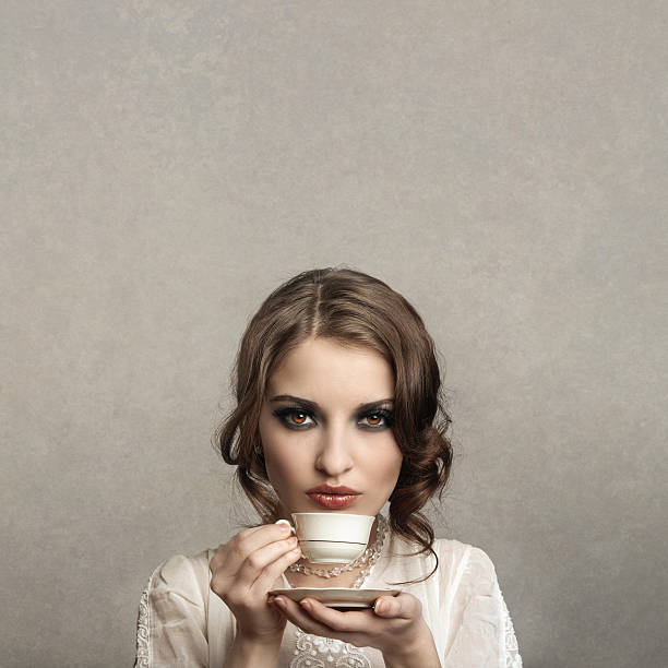 Dreamy model drinking tea resting cityscape rooftop in front sunset sky closeup. Mysterious serene brunette looking camera relaxing at balcony alone portrait. Tranquil woman sipping coffee at terrace