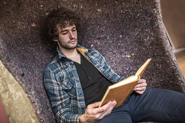 istock Young man relaxing in armchair and reading a book. 487686134