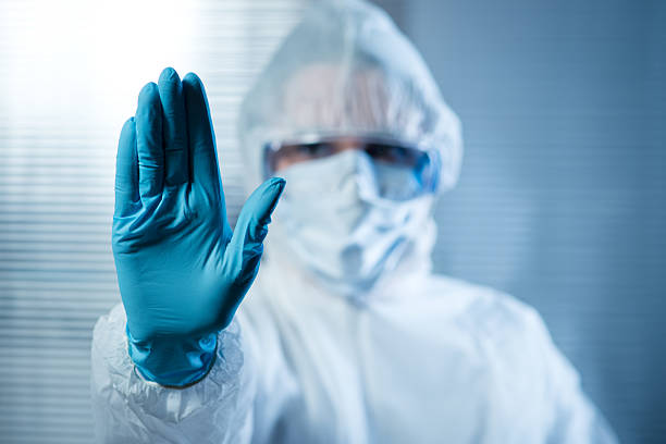 Female scientist in protective hazmat suit with hand raised Scientist with hand raised in hazmat protective suit, stop concept. biological warfare stock pictures, royalty-free photos & images