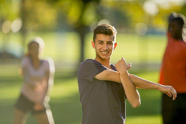 Man Stretching His Arms at the Park A multi-ethnic group of teenagers are outside at a park stretching on a beautiful sunny day. One man is smiling and looking at the camera. military camp stock pictures, royalty-free photos & images