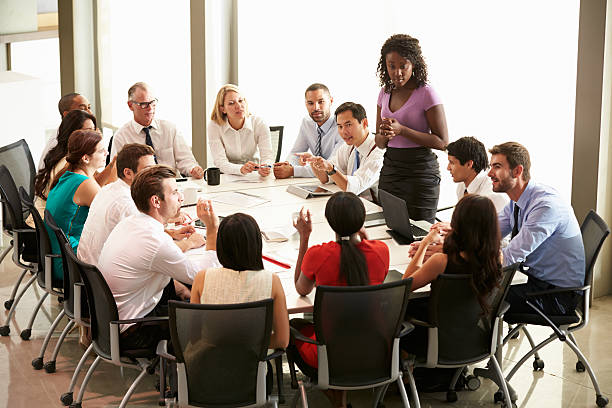 Businesswoman addressing others around board table Businesswoman Addressing Work Colleagues In Meeting Around Boardroom Table formal businesswear stock pictures, royalty-free photos & images