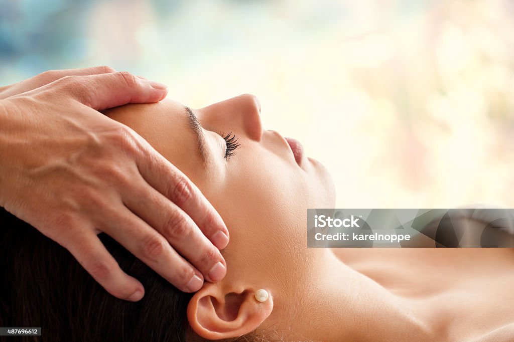 Woman having facial massage. Close up head portrait of young woman having facial massage in spa. Therapist massaging womans head against colorful background. Massaging Stock Photo