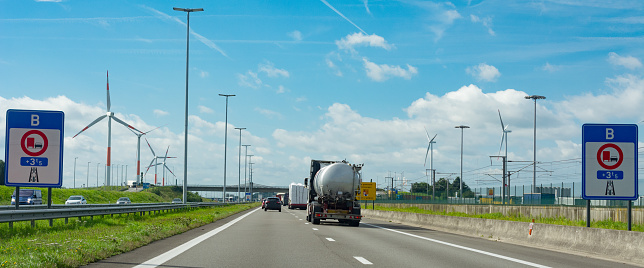 pov driving on a freeway, with wind turbines on both sides, into Belgium, ready to pass a tank truck in the direction of the Antwerp harbor