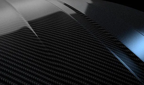 An abstract section of the contours of a carbon fibre automobile bonnet with dramatic lighting on a dark studio background