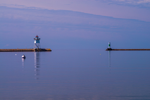 calm morning waters reflect grand marias lighthouse, in grand marais harbor, minnesota.