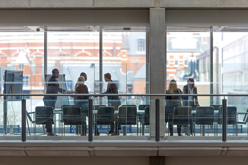 Group of six business people in a boardroom meeting. Shot at a distance from outside through the glass.