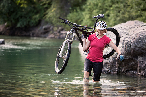 A female mountain biker carrying her bike across a stream.