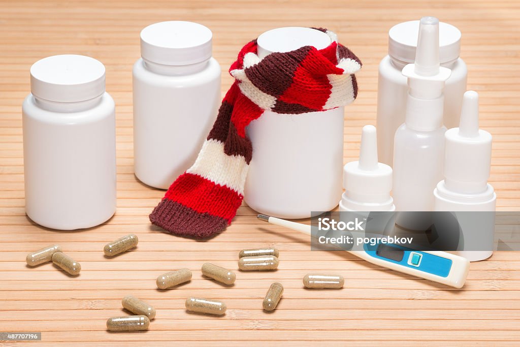 Set of various cold remedies Treatment of colds and flu concept. Jar of pills, tied with knitted scarf, surrounded by jars of medicines, scattered capsules, electronic thermometer, nasal sprays 2015 Stock Photo