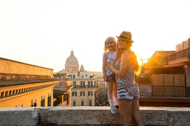 istock Mother holding daughter standing on ledge at sunset in Rome 487719036