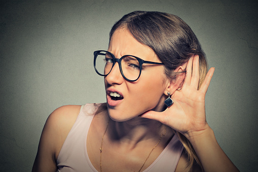 Closeup portrait young nosy woman hand to ear gesture trying carefully intently secretly listen in on juicy gossip conversation news  isolated gray background. Human face expression. Hard to hear