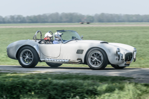 Ens, The Netherlands - April 20, 2014: Two people driving on a country road in a classic Ford/Shelby AC Cobra sports car on a beautiful spring day.