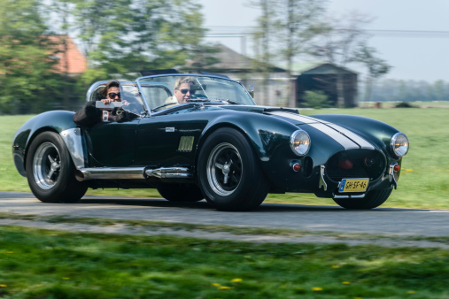 Ens, The Netherlands - April 20, 2014: Two people driving on a country road in a classic Ford/Shelby AC Cobra sports car on a beautiful spring day.