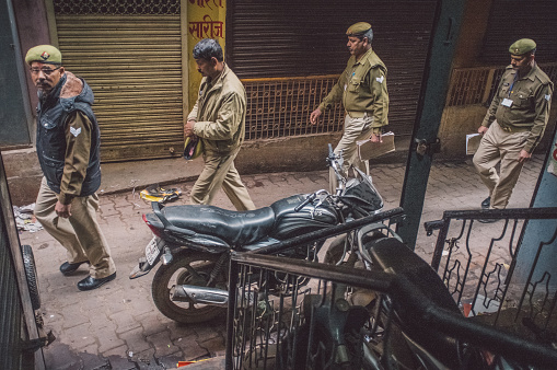 Varanasi, India - February 20, 2015: Four Indian policemen walk on street of old part of Varanasi and pass by parked motorcycle. Post-processed with grain, texture and colour effect.