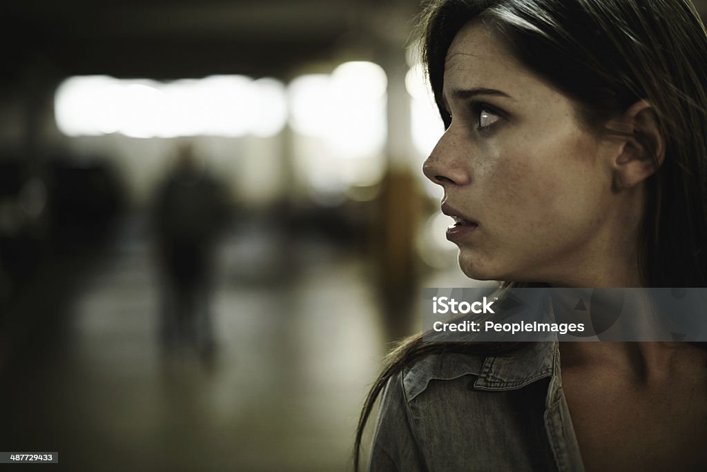 Something's not right here... A terrified young woman in an underground parking garage being followed by a sinister man Fear Stock Photo