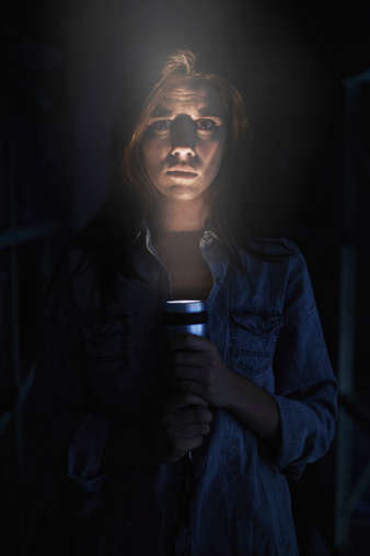 A young woman looking serious while holding her flashlight in the dark
