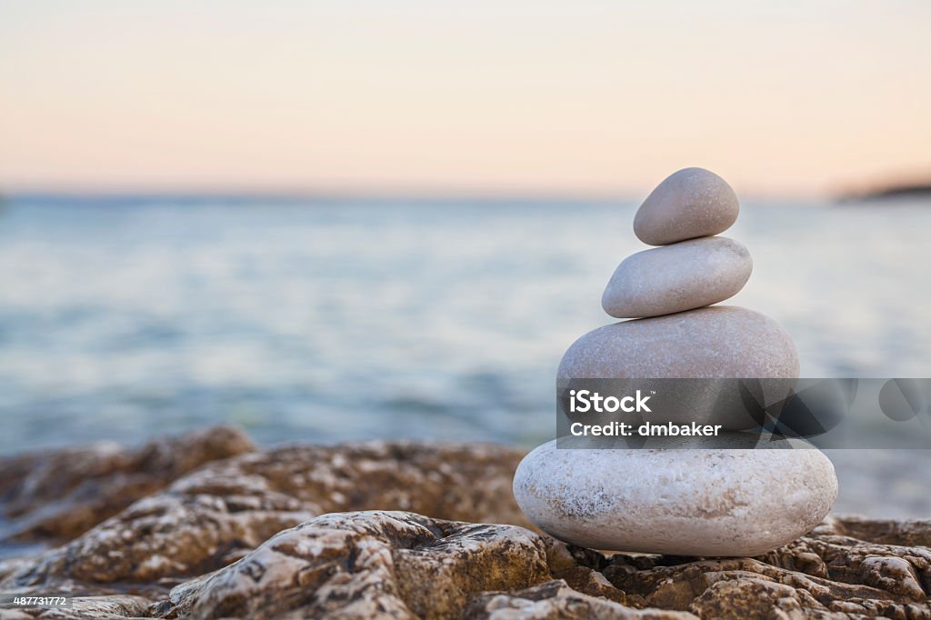 Pile of Stones on Tranquil Beach at Sunset Tower of stones piles on top of a rock on a tranquil deserted beach at evening sunset Stone - Object Stock Photo