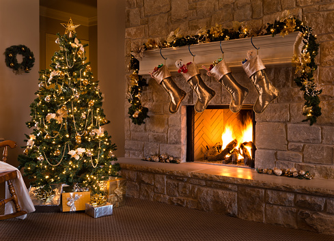 A beautiful contemporary gold-themed Christmas Eve fireplace, tree, stockings, and living room. Stockings hanging from mantel by fireplace, and gifts under tree.