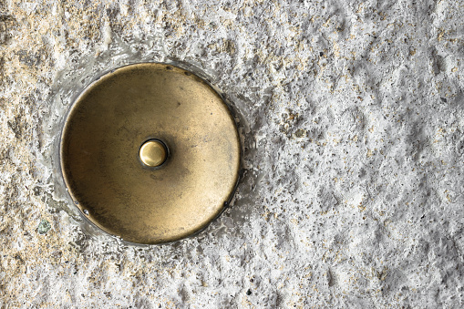 Extreme close-up of an old doorbell copper, on rough plaster.