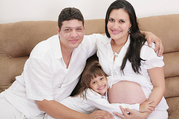 Portrait of a young father posing with his adorable daughter and his pregnant wife in an advanced state of pregnancy.
