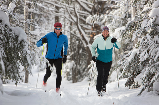 A man and woman cross country skiing on a snowy trail in the midwest.