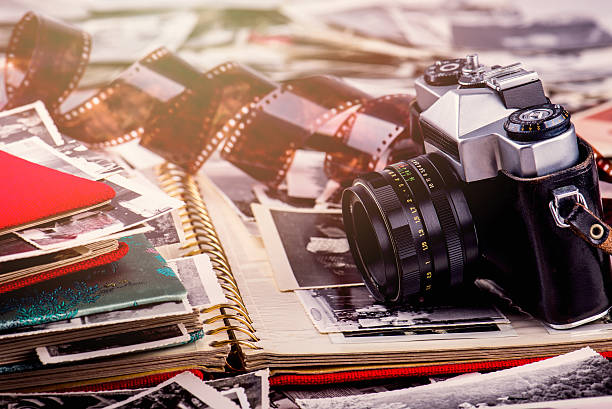 Vintage photo camera and photo album Analogue camera surrounded with old images and photo albums, little flare. shallow DOF. old black leather photo album stock pictures, royalty-free photos & images