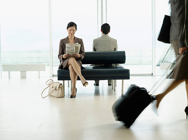 Businesswoman Reading Newspaper At Airport Lobby Businesswoman sitting on bench and reading newspaper in airport newspaper airport reading business person stock pictures, royalty-free photos & images