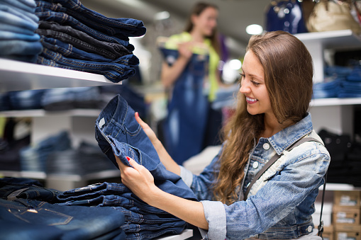 Joyful smiling young longhaired girl choosing new jeans at store