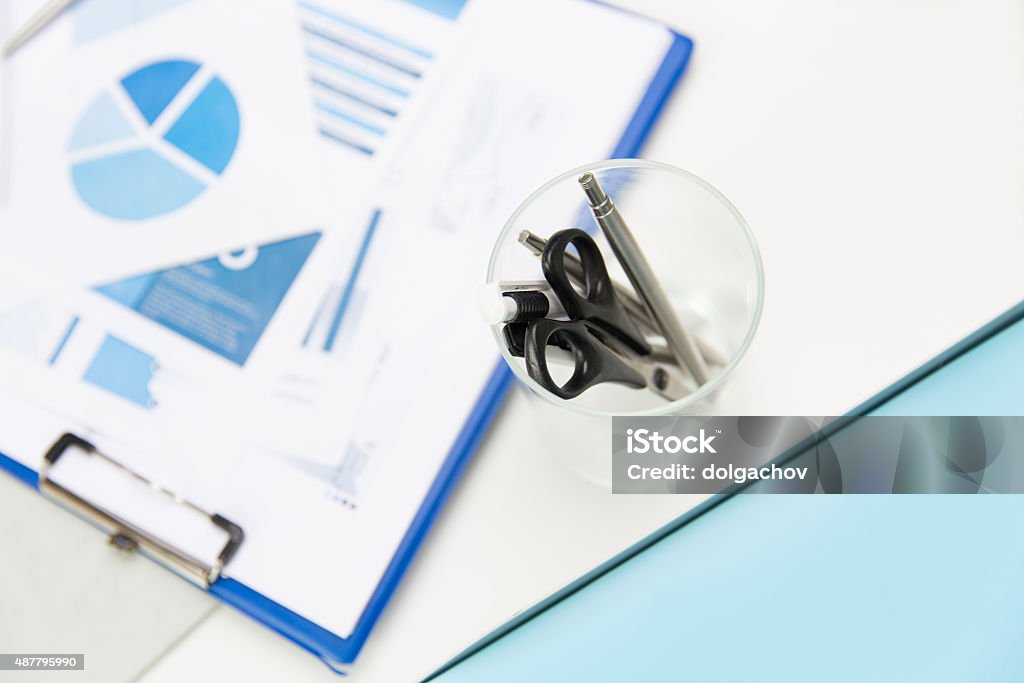 close up of cup with scissors and pens at office business, stationery and office supply concept - close up of organizer with scissors and pens over charts on table 2015 Stock Photo