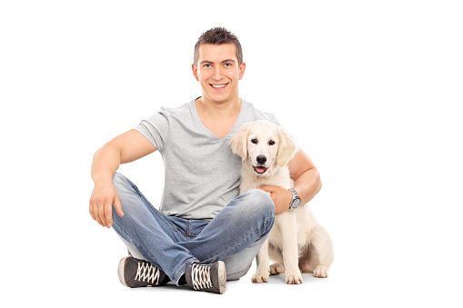 Young man sitting on the floor and hugging a Labrador puppy isolated on white background