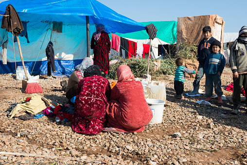 Atmeh, Syria - January 14, 2013: Syrian woman wash clothes outdoors as children stand nearby in the displaced persons camp in Atmeh, Syria.