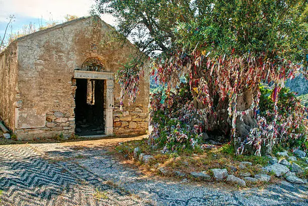 Photo of old abandoned church with big olive tree and colourful rags
