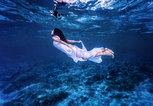 Swimming in beautiful blue sea, gentle woman in white fashion dress diving underwater, refreshment and enjoyment concept