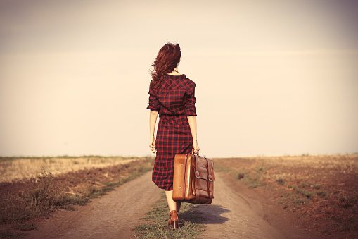 Beautiful girl in plaid dress with bag on countryside