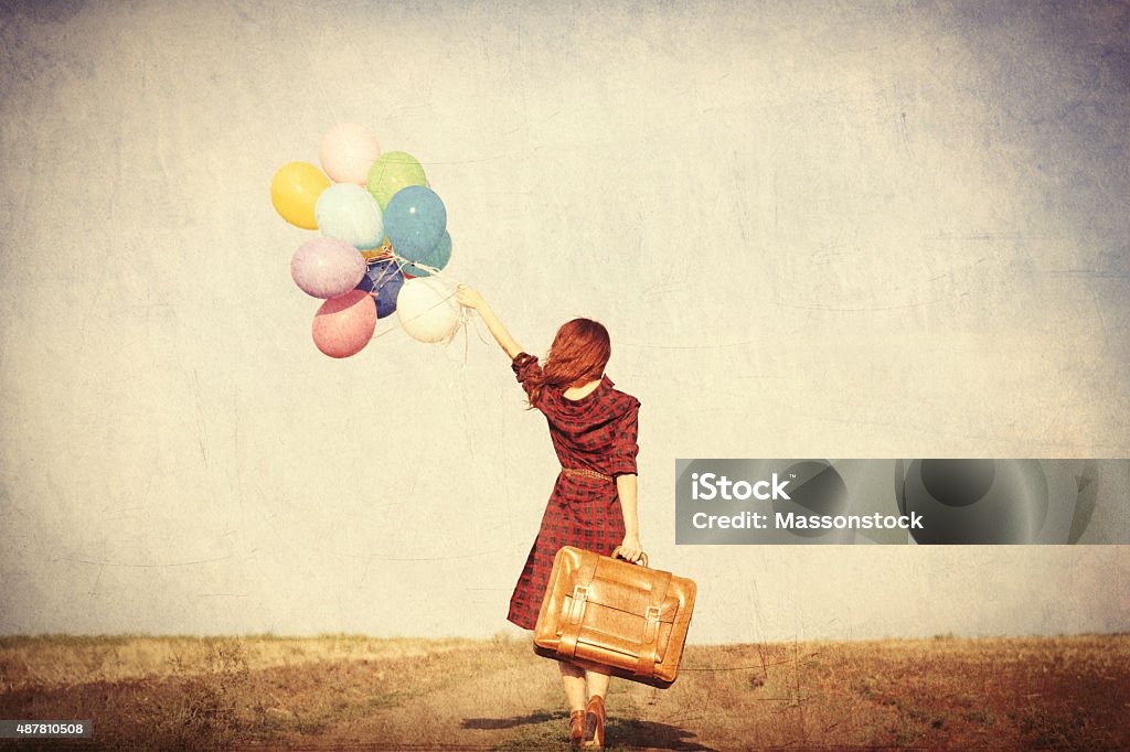 girl with multicolored balloons and bag Beautiful girl in plaid dress with multicolored balloons and bag on countryside Suitcase Stock Photo
