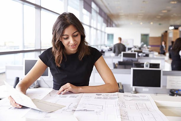 istock Young female architect working with blueprints in an office 487813960
