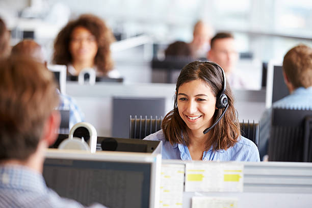 mujer joven trabajando en call centre, rodeado de sus colegas - centro de llamadas fotografías e imágenes de stock