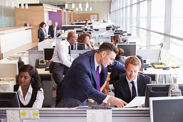 istock Two businessmen discussing work in a busy, open plan office 487814714