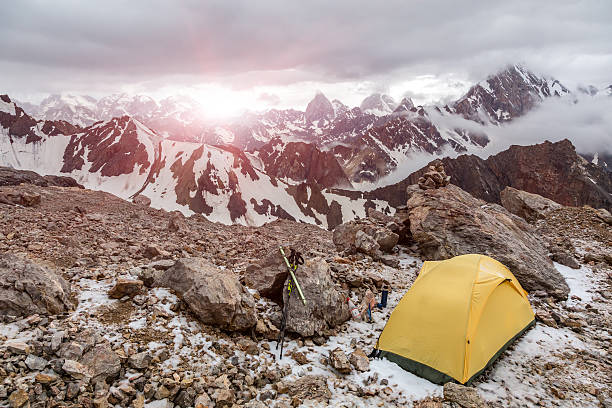 Small Alpine camping Tent located on rocky terrain stone surface and high mountain hills and peaks on background evening sun light