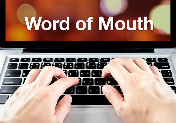 Photo of Word of mouth on notebook with hand type on keyboard