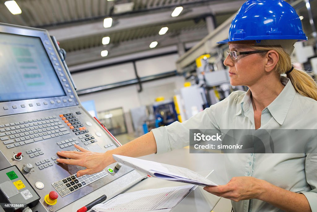 Programming A CNC Machine Female engineer programming a CNC machine at the manufacturing plant. Machinery Stock Photo