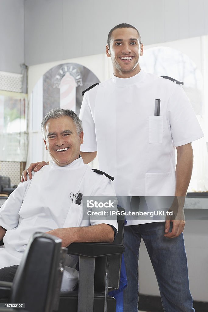 Barbers Smiling In Hair Salon Portrait of two barbers in uniforms smiling at hair salon Hair Salon Stock Photo